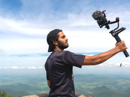 Homem jovem blogueiro com boné na montanha segurando a câmera gravando