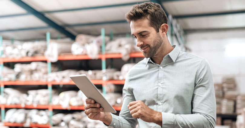 Empresário de e-commerce olhando para o tablet sorrindo dentro do estoque